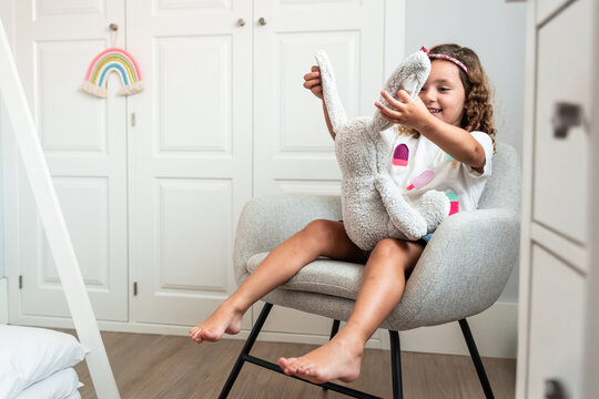 Happy little girl hugging stuffed bunny on chair at home