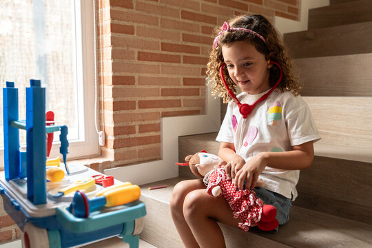 Child playing doctor with toy stethoscope at home by window