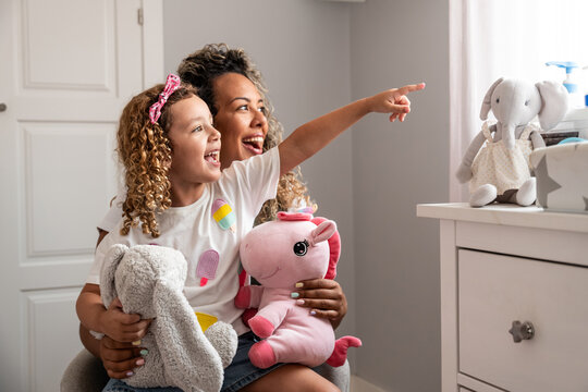 Mother and daughter pointing in nursery with plush toy