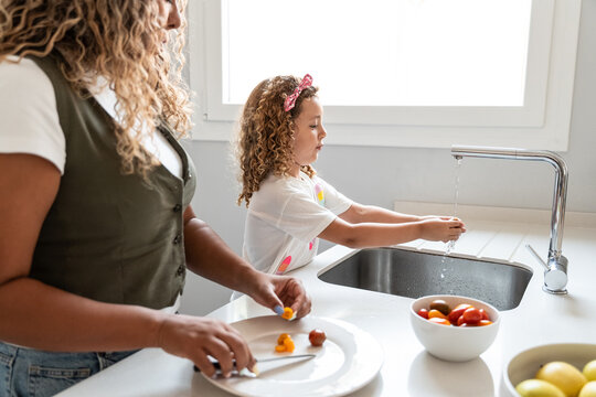 Child washing hands at kitchen sink while adult prepares food