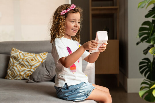 Young girl using calculator on sofa at home, smiling