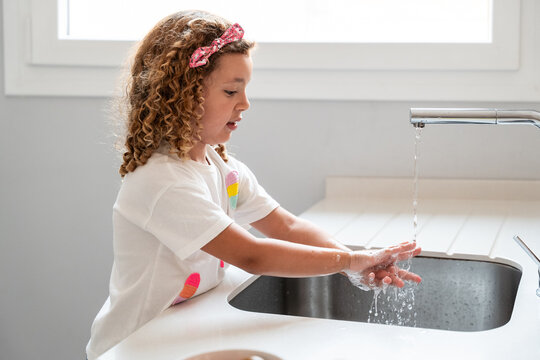 Child washing hands at kitchen sink with running water