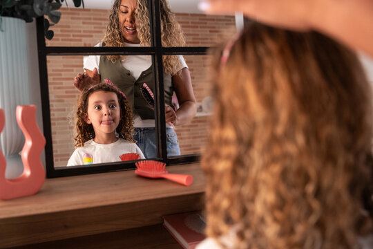Mother brushing daughter hair at home in front of mirror