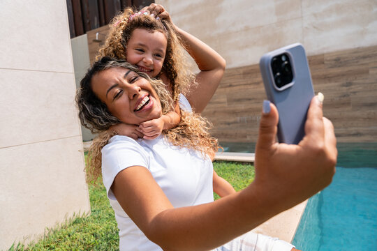 Mother and daughter taking selfie together by pool outdoors