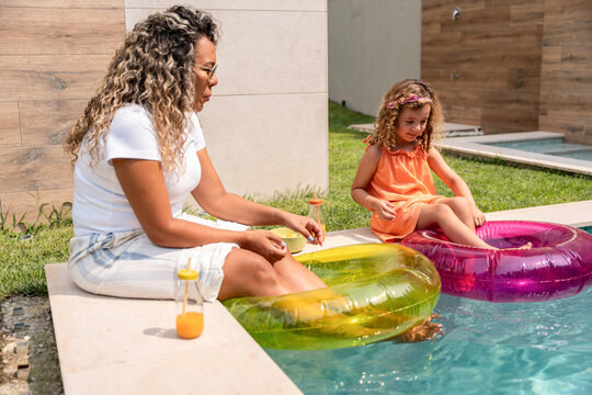 Mother and daughter relaxing with float rings by pool