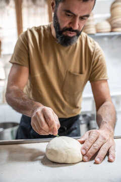 Baker scoring dough by hand in an artisan bakery kitchen