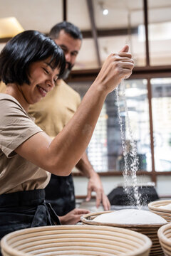 Artisan baker dusting flour over dough in bakery kitchen