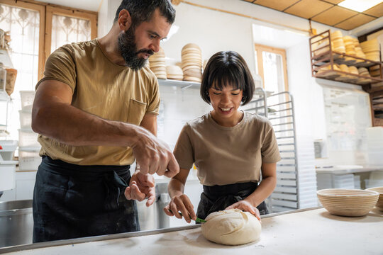 Baker coaching apprentice shaping dough in artisan bakery