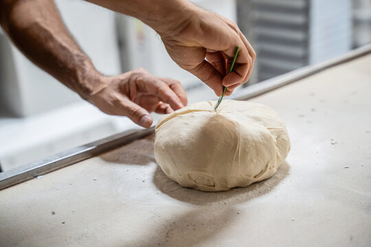 Artisan baker scoring dough by hand on a bakery table