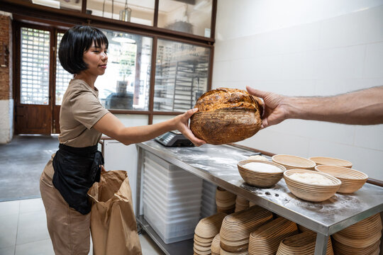 Baker handing sourdough loaf to customer in bakery
