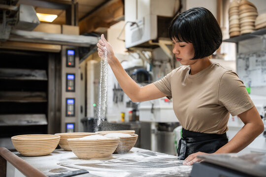 Baker dusting flour over dough in artisan bakery kitchen