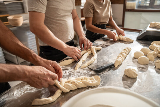 Bakers shaping braided dough at artisan bakery worktable