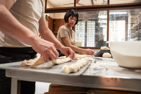 Artisan bakery staff shaping dough on stainless worktable