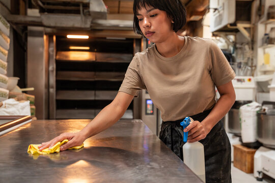 Baker cleaning stainless table in artisan bakery kitchen
