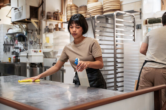 Artisan bakery worker sanitizing stainless steel counter