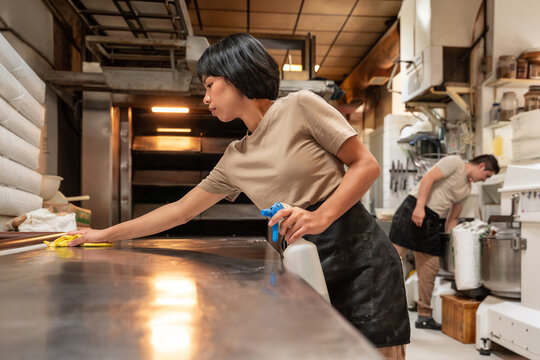 Baker cleaning stainless steel table in artisan bakery kitchen