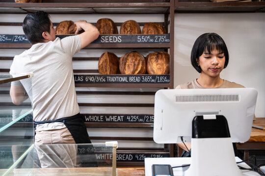 Artisan bakery staff arranging bread while cashier works