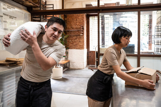 Bakery staff handling flour sack and boxes in busy kitchen