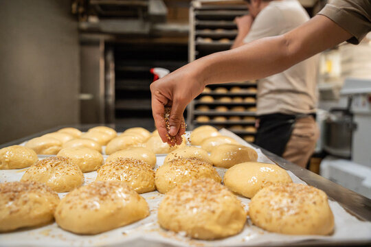 Baker sprinkling seeds on fresh dough rolls in bakery