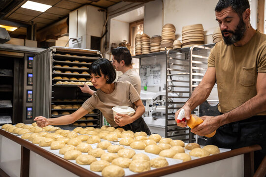 Bakers glazing dough pieces in an artisan bakery kitchen
