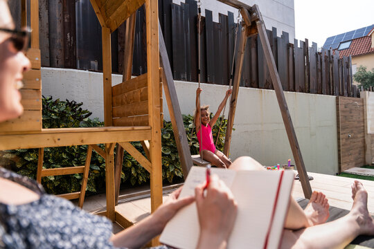Mother relaxing on deck while daughter swings outdoors