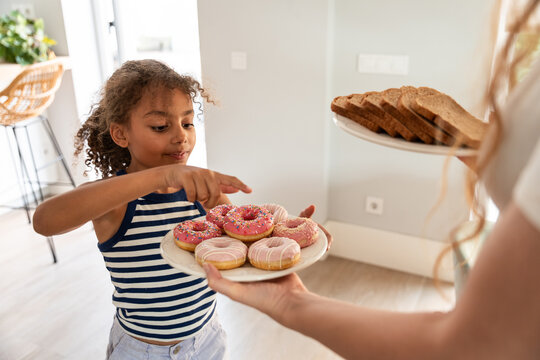 Mother and daughter choosing donuts and toast in kitchen