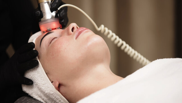 Female client enjoying RF lifting facial procedure in aesthetic clinic. Skincare concept.
