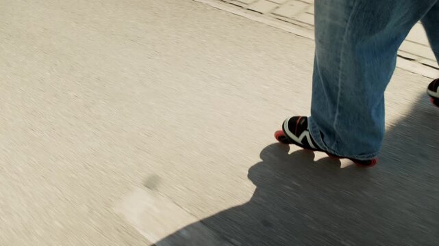 Gimbal side tracking shot of inline skates with red wheels gliding on sunny promenade. Dramatic full body skater shadow across concrete, white road marking, motion blur. Dynamic urban active sport 