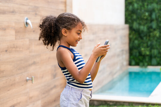 Young girl using smartphone near outdoor swimming pool