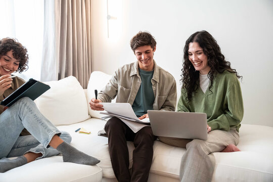 Young adult friend group studying on sofa with laptop