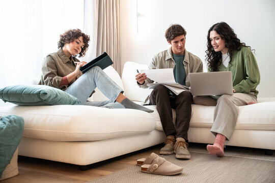 Young adult reviewing document and laptop on living room sofa