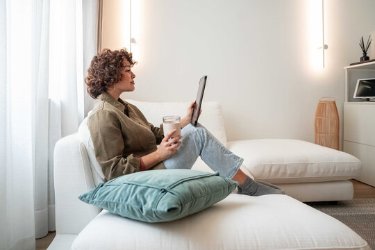 Woman relaxing on sofa with tablet and coffee at home