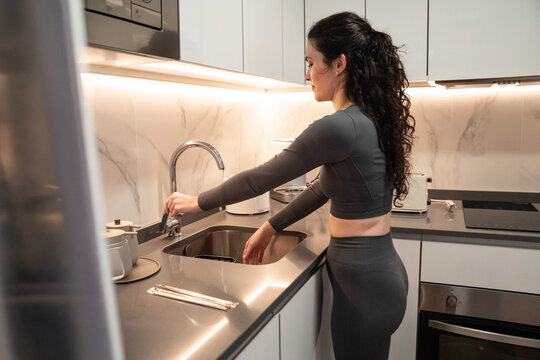 Woman washing hands at modern kitchen sink at home