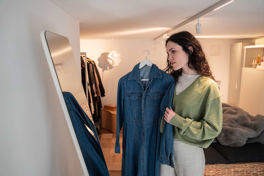 Woman choosing denim dress in bedroom wardrobe by mirror
