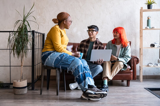 Diverse friends chatting with laptop on loft room sofa