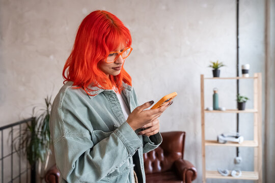 Red haired woman using smartphone in modern home interior