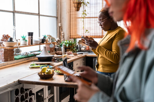 Two women using smartphone in cozy kitchen at home