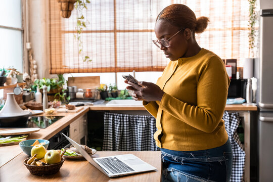 Woman using smartphone while working in home kitchen