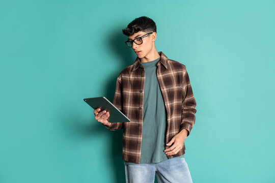 Young man with glasses using tablet on teal background