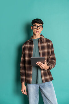 Young man holding tablet in studio portrait on teal wall