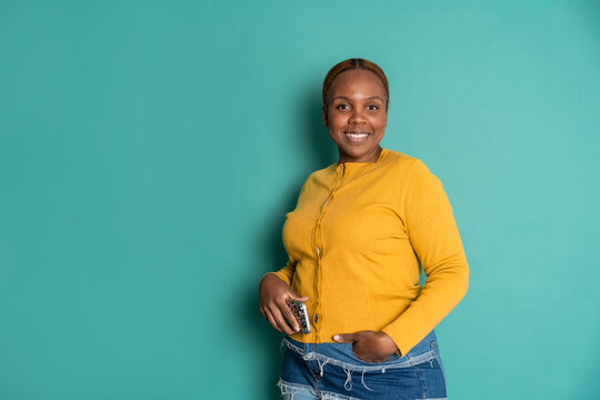 Smiling woman in yellow sweater holding phone on teal wall