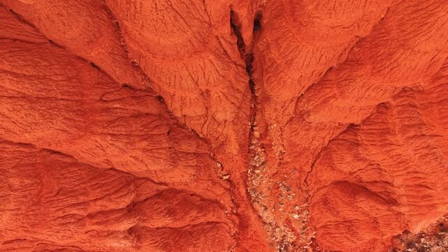 Top-down drone view of red clay ravine. Vertical drone view of red eroded clay ravine with narrow channel, loose stones, and steep walls.