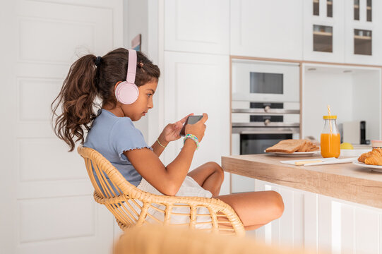 Hispanic girl using smartphone with headphones at breakfast table