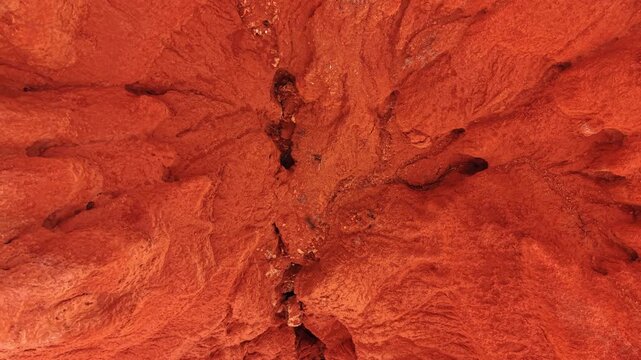 Overhead view of eroded red gullies and ravine. Overhead drone view of red clay badlands with branching gullies, rock debris, and textured slopes.