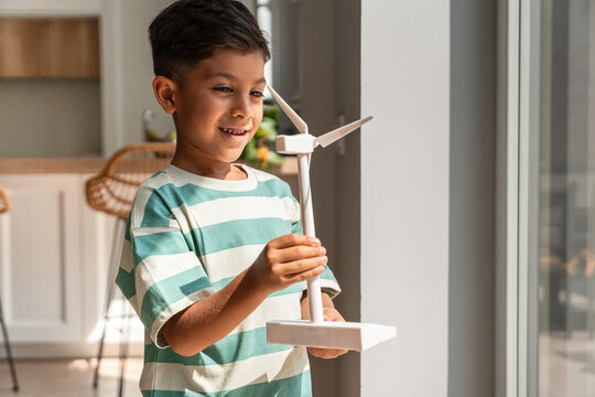 Smiling Hispanic boy holding wind turbine model at home