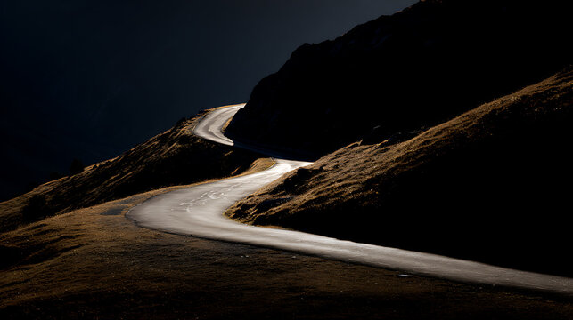 Dramatic alpine road winding through dark mountain peaks, bathed in a sliver of golden light, showcasing contrast and adventure in nature's heart
