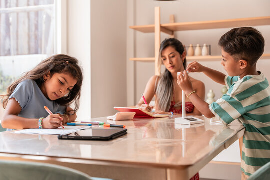 Hispanic family helping kids study at home at kitchen table
