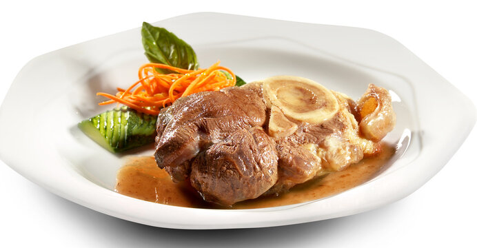 Braised beef osso buco with marrow bone served on a white plate with carrot and cucumber garnish