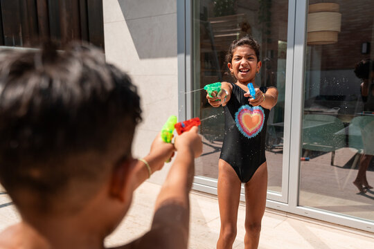 Hispanic siblings water fight with toy guns in backyard