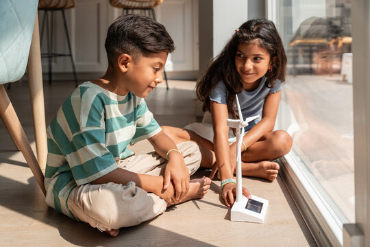 Hispanic siblings exploring renewable energy with wind toy